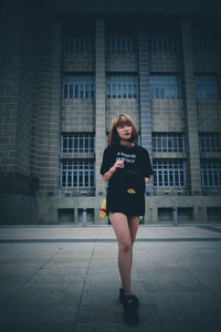 Portrait of young woman standing against building in city