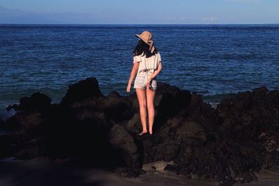 Rear view full length of woman standing on rocky shore