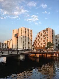 Bridge over river by buildings in city against sky