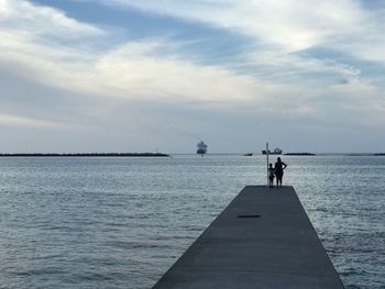 People standing on jetty by sea against sky