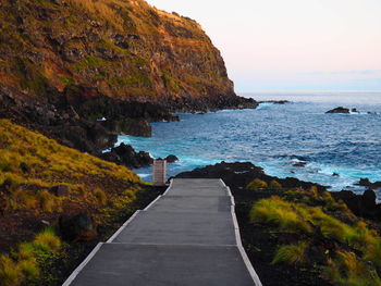 Scenic view of sea by mountain against sky