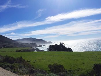 Scenic view of green landscape and sea against sky