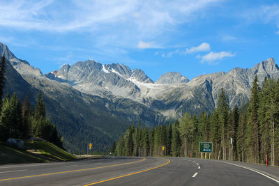 Road amidst trees and mountains against sky