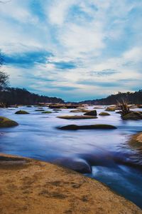 Rocks amidst flowing river against sky