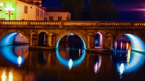 Arch bridge over river in city at night