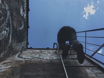 Low angle view of man climbing ladder on building against sky