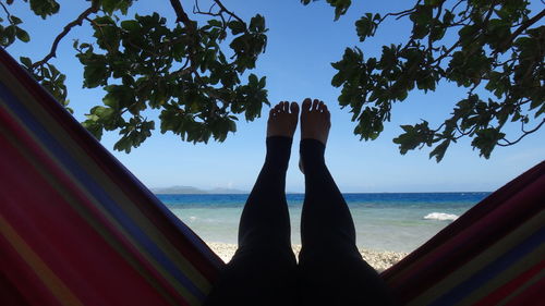 Low section of man relaxing by sea against sky
