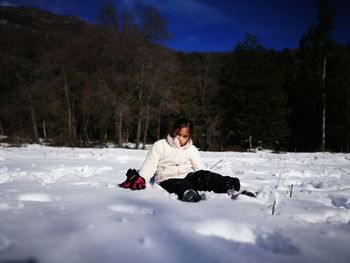 Full length of girl sitting on snow covered landscape