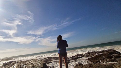 Rear view of young woman at beach against sky