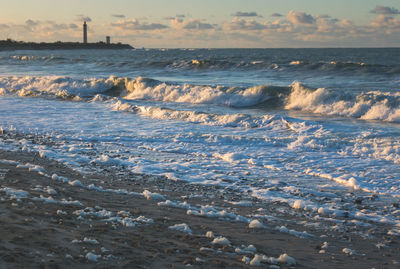 Waves rushing towards shore against sky