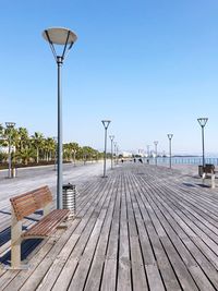 Empty footpath by pier against clear blue sky