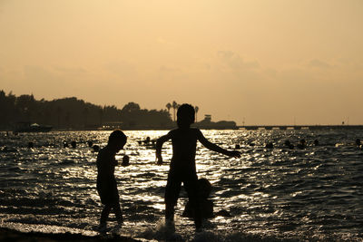 Silhouette kids playing at beach against sky during sunset
