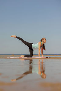 Side view of woman exercising at beach against clear sky