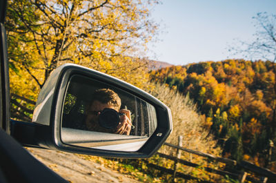 Reflection of man photographing from camera on side-view mirror of car