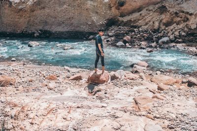 Full length of man standing on rock by river during sunny day