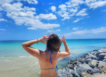 Rear view of woman standing at beach against blue sky
