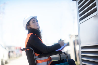 Young technician with safety helmet and vest in wheelchair working outdoors