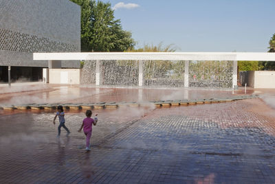 People at fountain in city against sky