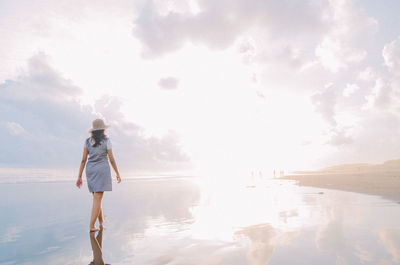 Rear view of woman walking at beach against sky