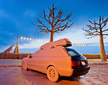 Snow covered vehicle by bare trees
