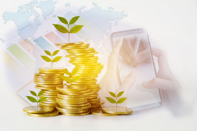 Digital composite image of hand using mobile phone with holding glass of coins and plants on table