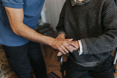 Midsection of male care assistant holding hands of senior man at home