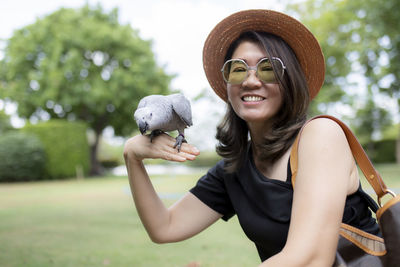 Portrait of smiling young woman holding parrot outdoors