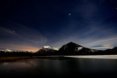 Scenic view of lake and rocky mountains against sky at night