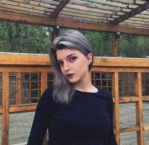 Portrait of young woman standing against wooden railing