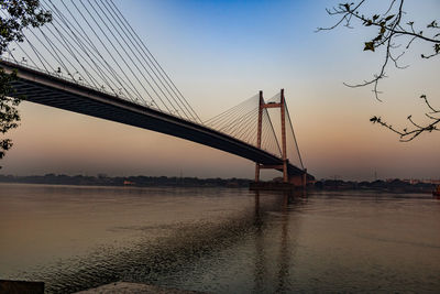 Suspension bridge over river during sunset