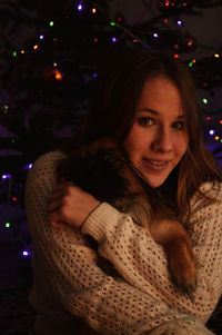 Portrait of smiling young woman hugging dog against the christmas tree