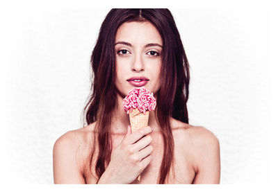 Portrait of beautiful woman holding ice cream while standing against white background