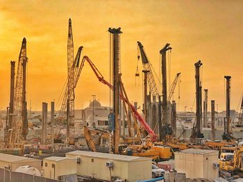 Cranes at construction site by buildings against sky during sunset
