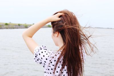 Woman with hand in hair at beach against sky