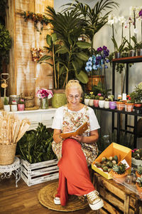 Female florist writing in book while sitting in flower shop