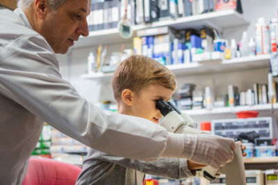 Side view of engineer assisting boy in looking through microscope