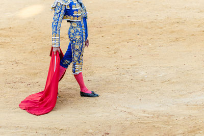 Crop of unrecognizable bullfighter in traditional costume holding estoc sword and capote while performing on bullfighting arena