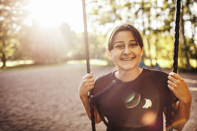 Portrait of smiling teenage girl sitting on swing at playground