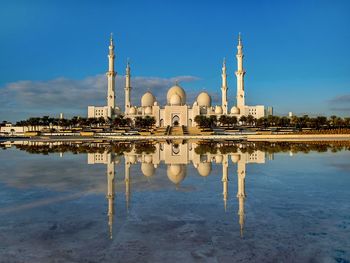 Reflection of mosque in lake against blue sky