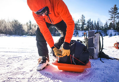 A man packs up a pulk sled in a snowy parking lot