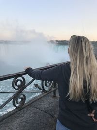 Rear view of woman by waterfall against sky