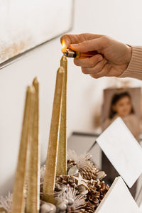 Crop unrecognizable person lighting decorative candle among coniferous cones while celebrating new year holiday in house person