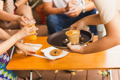 Waitress serving hot latte coffee to customer at cafe.