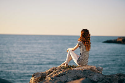 Woman on rock by sea against clear sky