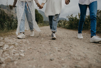Low section of friends holding hands while walking on dirt road