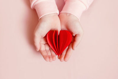 Closeup of child kid hands holding red folded heart on light pink background. valentines day holiday