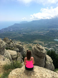 Rear view of woman sitting on rock against mountain