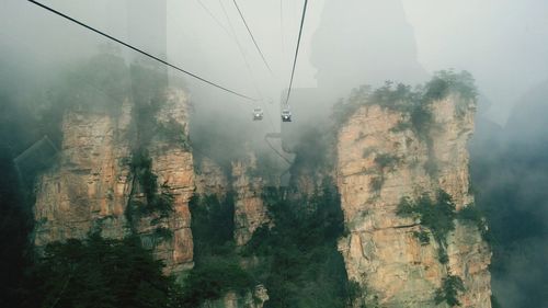 Overhead cable cars amidst rocky mountains during foggy weather