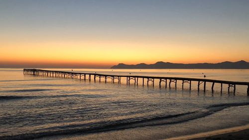 Pier over sea against clear sky during sunset