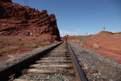 Railroad tracks leading towards mountains against clear sky